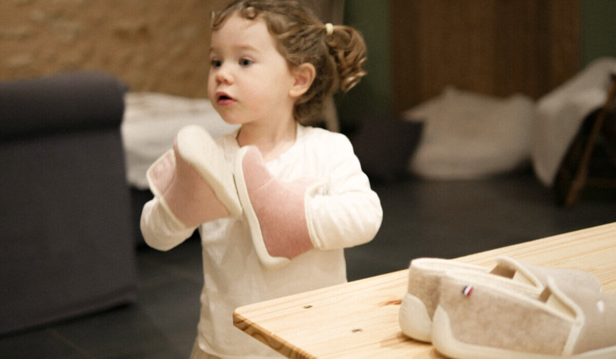 Petite fille tenant ses chaussons Hellocotton dans ses mains et les tapant comme un instrument de musique, illustrant le jeu et la curiosité des bébés