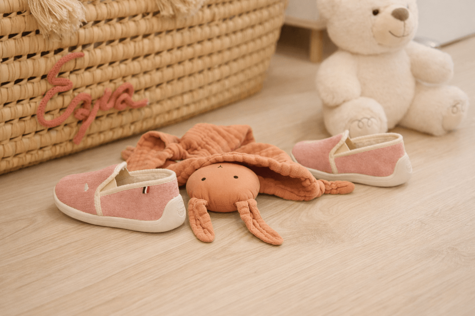 Chaussons bébé souples placés au sol à côté d’un doudou, illustrant le confort et la sécurité des pieds des tout-petits